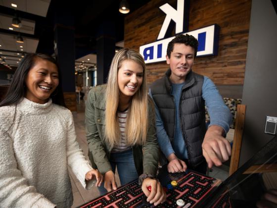 A group of students play pac-man on an arcade machine in K-Lair.